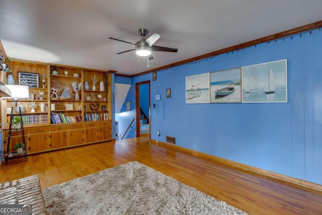 sitting room with wood-type flooring, built in features, crown molding, and ceiling fan