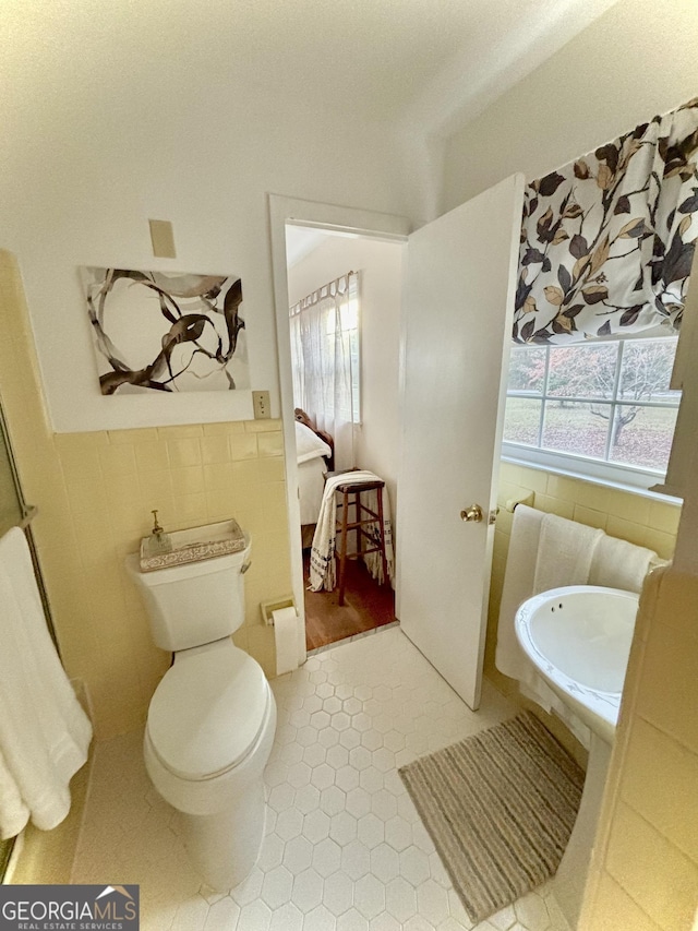 bathroom with toilet, tile patterned flooring, and tile walls