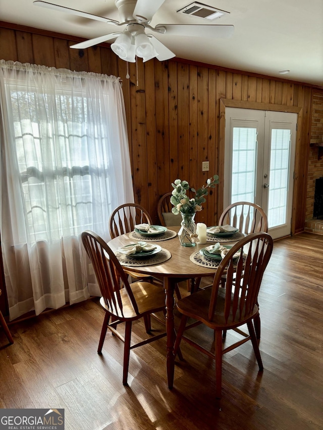 dining space featuring hardwood / wood-style floors, wood walls, ceiling fan, and french doors