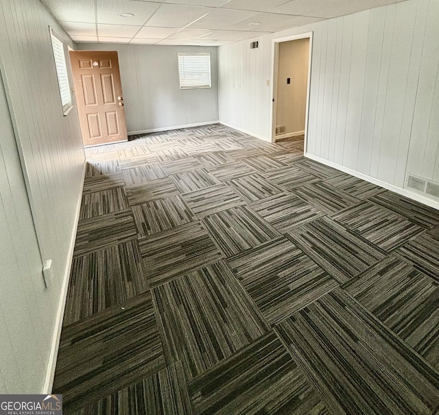 unfurnished room with wooden walls and a drop ceiling