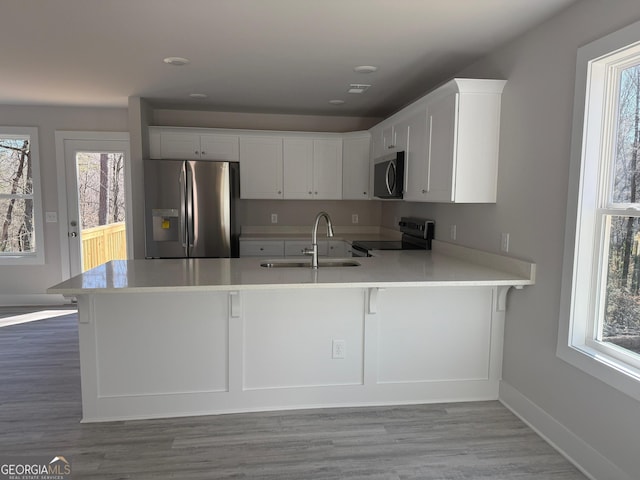 kitchen featuring sink, stainless steel appliances, white cabinetry, and kitchen peninsula