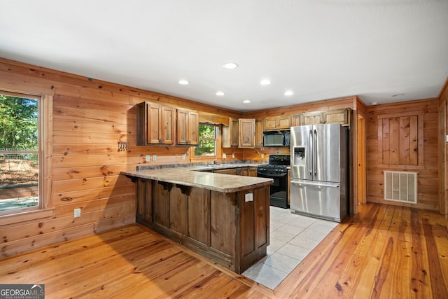 kitchen featuring wooden walls, light hardwood / wood-style flooring, kitchen peninsula, and black appliances