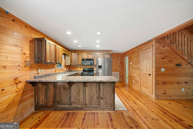 kitchen featuring light hardwood / wood-style floors, wood walls, kitchen peninsula, and black appliances