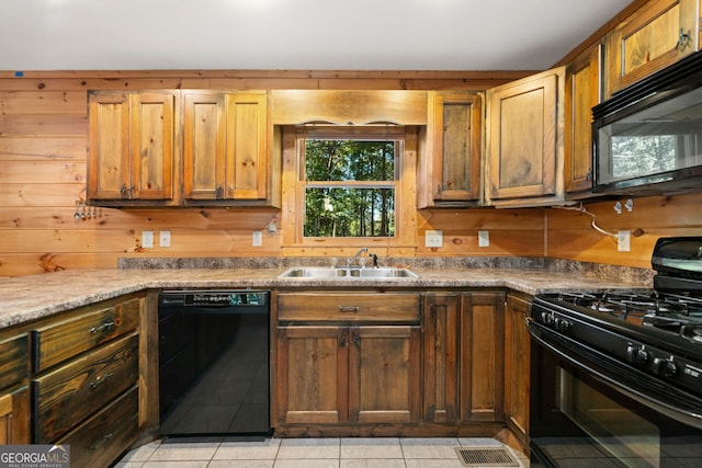 kitchen with light tile patterned flooring, black appliances, wooden walls, and sink