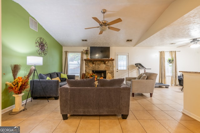 tiled living room featuring a stone fireplace, a textured ceiling, lofted ceiling, and ceiling fan