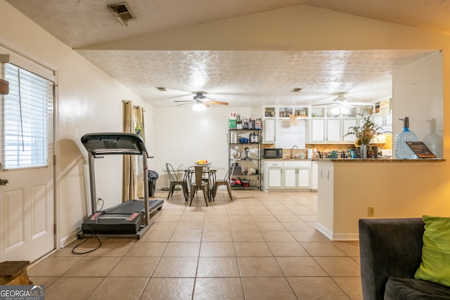 workout area with ceiling fan, a textured ceiling, light tile patterned floors, and lofted ceiling