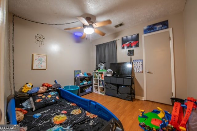 bedroom with hardwood / wood-style floors, ceiling fan, and a textured ceiling