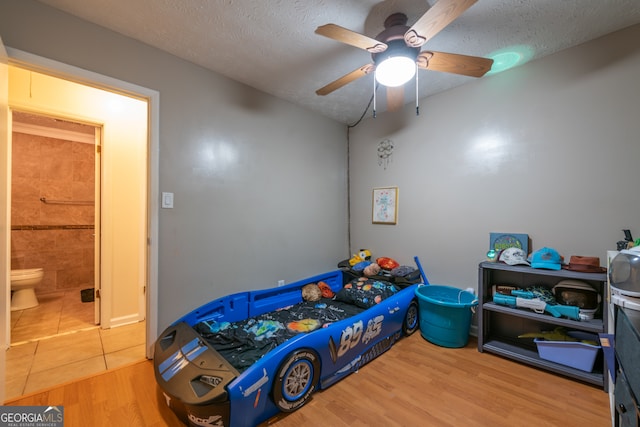 bedroom featuring connected bathroom, hardwood / wood-style floors, a textured ceiling, and ceiling fan