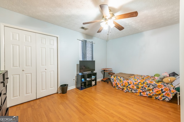 bedroom with a textured ceiling, wood-type flooring, ceiling fan, and a closet