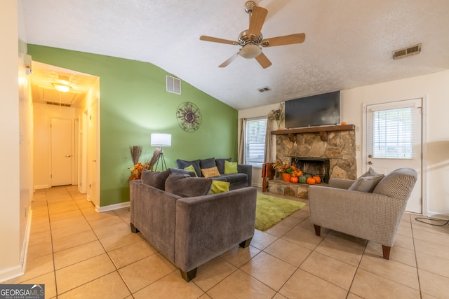 tiled living room featuring a textured ceiling, vaulted ceiling, ceiling fan, and a fireplace