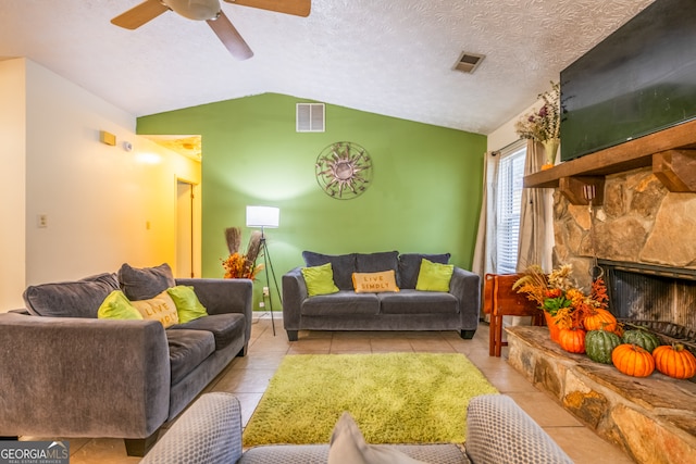 tiled living room featuring a stone fireplace, a textured ceiling, ceiling fan, and vaulted ceiling