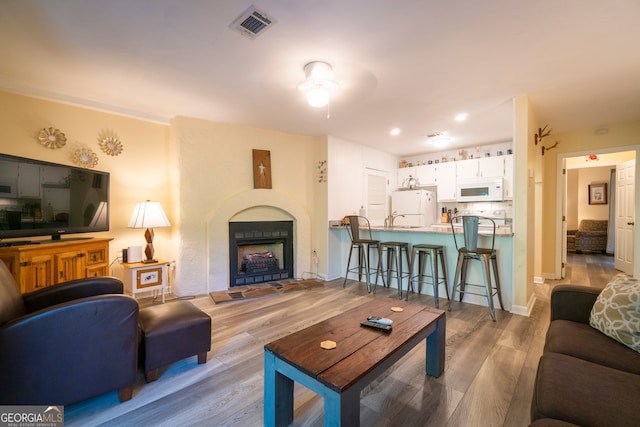 living room with ceiling fan, light wood-type flooring, and a tiled fireplace