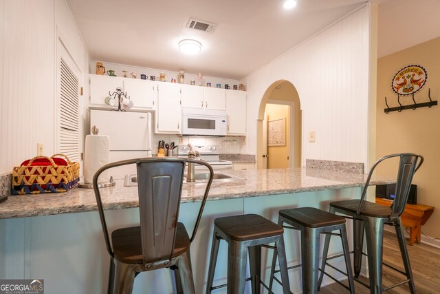 kitchen with light stone counters, white cabinets, dark hardwood / wood-style flooring, and white appliances