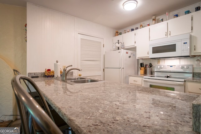 kitchen with light stone countertops, white cabinetry, white appliances, and sink