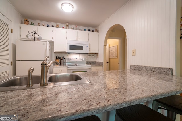 kitchen featuring kitchen peninsula, sink, white appliances, white cabinetry, and a kitchen breakfast bar