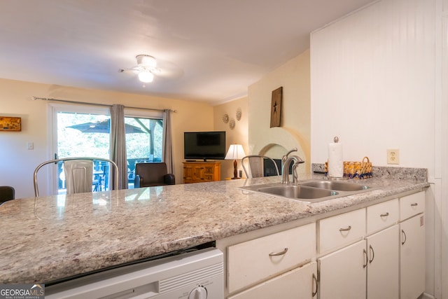 kitchen with ceiling fan, sink, light stone counters, kitchen peninsula, and white cabinets