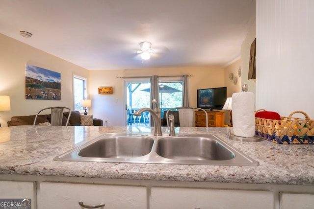 kitchen featuring ceiling fan, light stone countertops, and sink