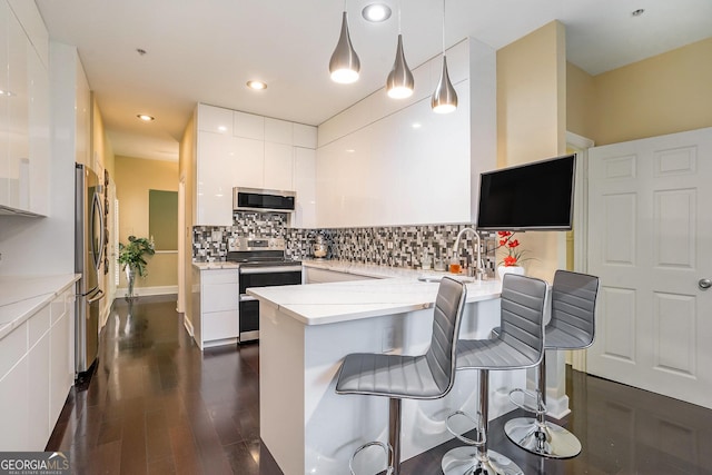 kitchen with sink, white cabinetry, stainless steel appliances, decorative light fixtures, and kitchen peninsula