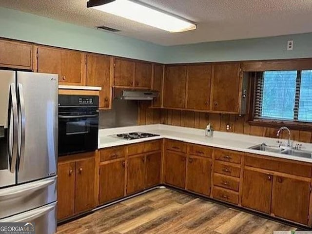 kitchen with black oven, stainless steel fridge with ice dispenser, under cabinet range hood, gas cooktop, and a sink