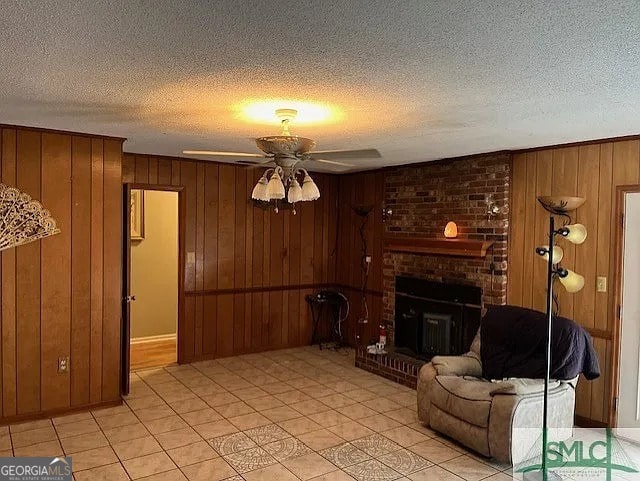 tiled living room featuring wooden walls, ceiling fan, a textured ceiling, and a brick fireplace