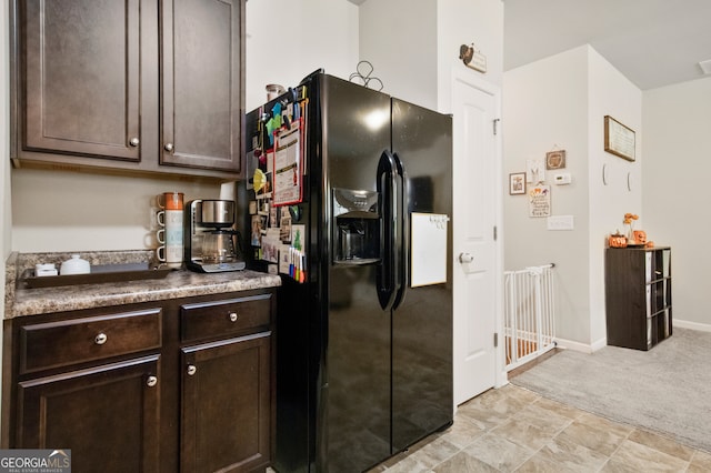 kitchen featuring light colored carpet, black fridge with ice dispenser, and dark brown cabinets