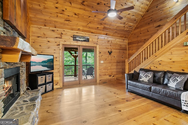 living room with light wood-type flooring, wooden ceiling, wooden walls, a stone fireplace, and high vaulted ceiling