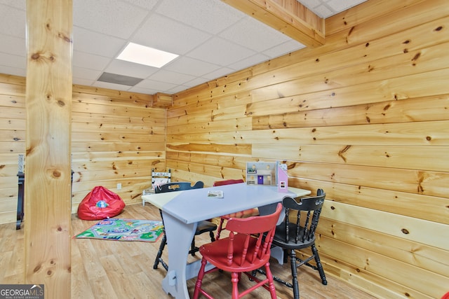 rec room with a drop ceiling, wooden walls, and hardwood / wood-style floors