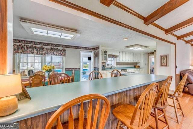 kitchen featuring white cabinets, beamed ceiling, a textured ceiling, crown molding, and light hardwood / wood-style floors