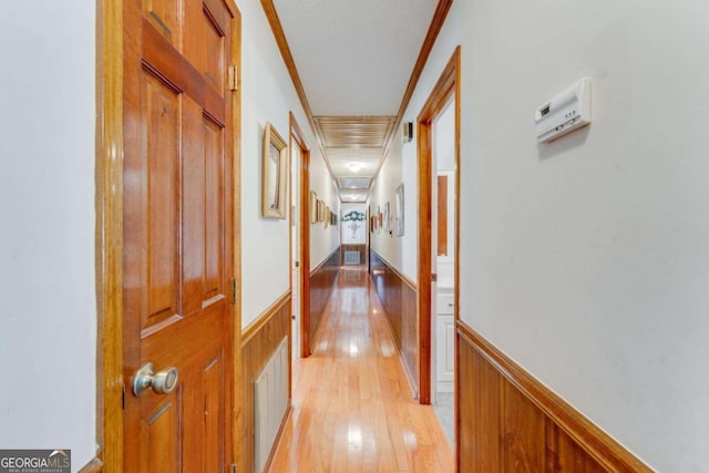 hall with ornamental molding, light wood-type flooring, and wooden walls