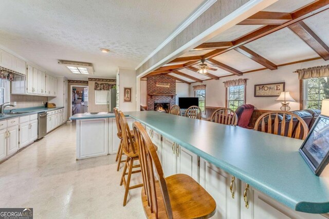 kitchen with ceiling fan, dishwasher, white cabinets, vaulted ceiling with beams, and a textured ceiling