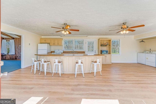 kitchen featuring light hardwood / wood-style floors, white appliances, independent washer and dryer, a kitchen bar, and a center island