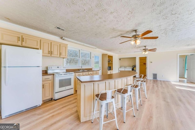 kitchen with a center island, white appliances, light hardwood / wood-style flooring, a kitchen bar, and a textured ceiling