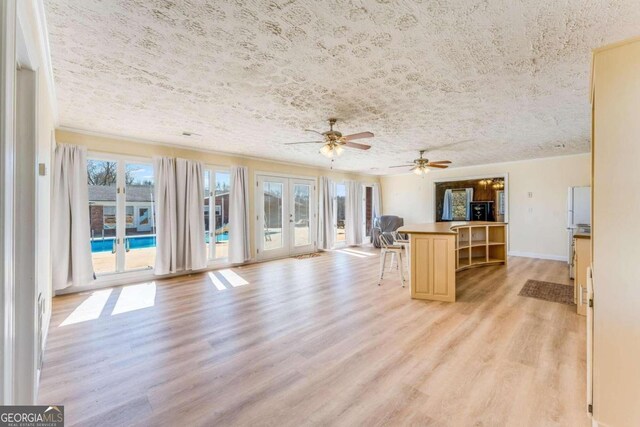 unfurnished living room with ceiling fan, french doors, light hardwood / wood-style floors, and a textured ceiling