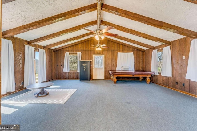 interior space featuring lofted ceiling with beams, carpet flooring, ceiling fan, wood walls, and a textured ceiling