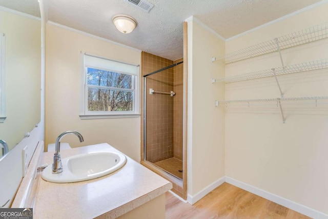 bathroom featuring vanity, hardwood / wood-style floors, a shower with door, ornamental molding, and a textured ceiling