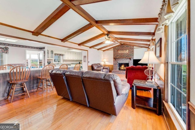 living room with ceiling fan, light wood-type flooring, lofted ceiling with beams, and a fireplace