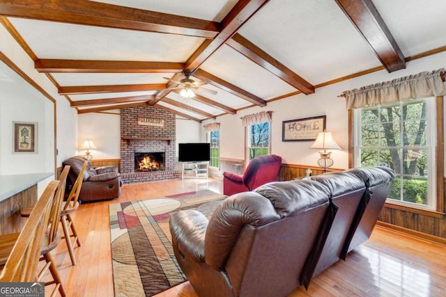 living room with a brick fireplace, ceiling fan, light hardwood / wood-style floors, vaulted ceiling with beams, and wood walls