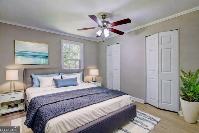 bedroom with ceiling fan, light wood-type flooring, two closets, and ornamental molding