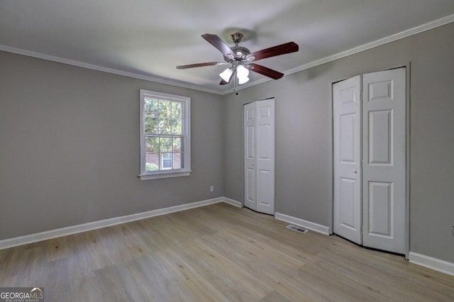 unfurnished bedroom with multiple closets, ceiling fan, crown molding, and light hardwood / wood-style floors