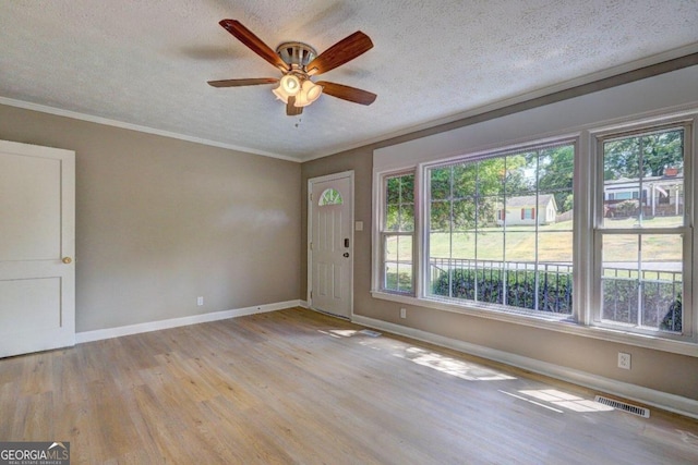 empty room featuring a textured ceiling, light wood-type flooring, ceiling fan, and crown molding