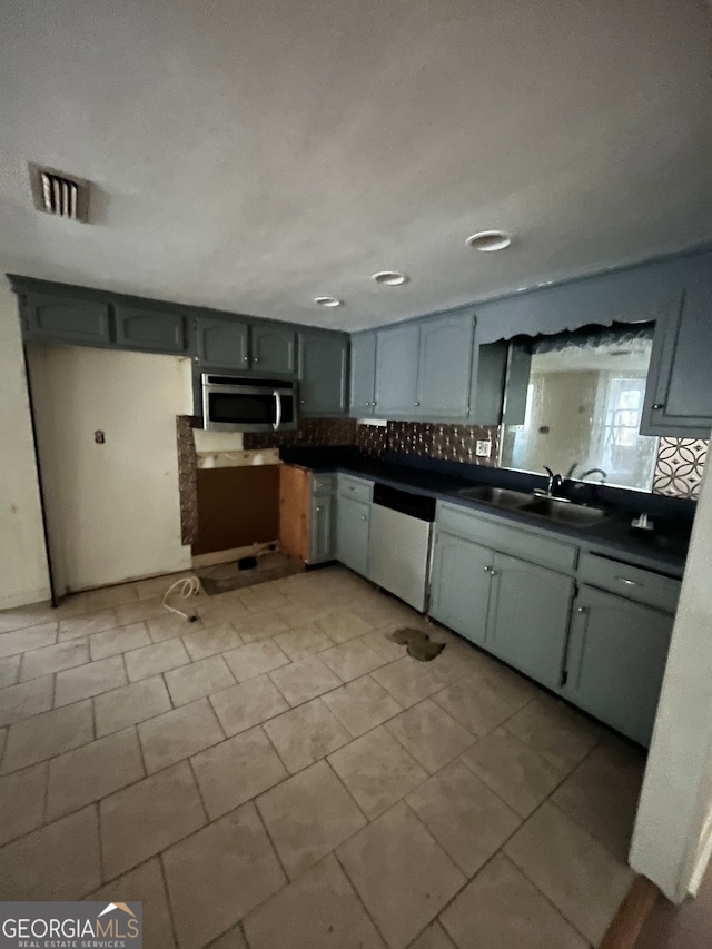 kitchen featuring tasteful backsplash, gray cabinets, dishwashing machine, and sink