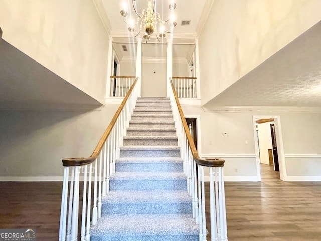 stairway with ornamental molding, hardwood / wood-style floors, and an inviting chandelier