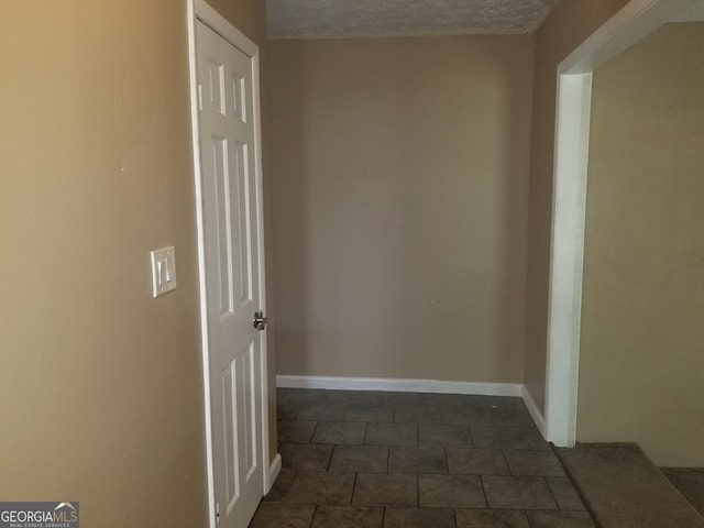 hallway featuring a textured ceiling and dark tile patterned floors