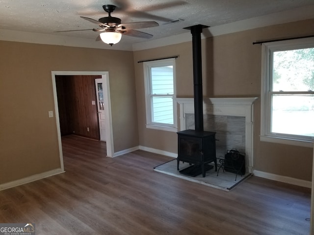 unfurnished living room featuring ceiling fan, hardwood / wood-style floors, a textured ceiling, and a wood stove