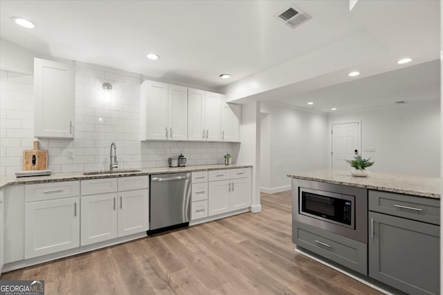 kitchen featuring light stone counters, white cabinets, sink, light hardwood / wood-style floors, and appliances with stainless steel finishes