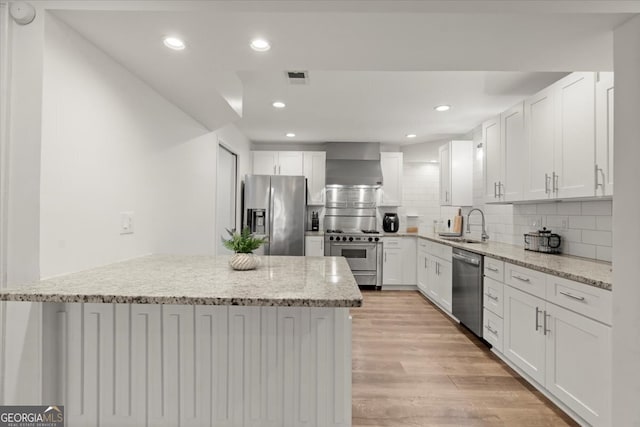 kitchen featuring light stone counters, wall chimney exhaust hood, white cabinetry, appliances with stainless steel finishes, and light hardwood / wood-style floors