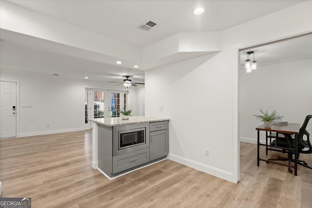 kitchen with pendant lighting, gray cabinetry, light stone countertops, stainless steel microwave, and light hardwood / wood-style floors