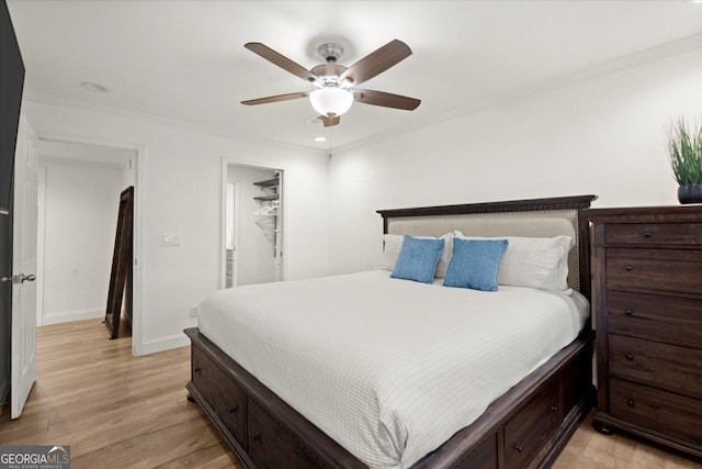 bedroom with light hardwood / wood-style floors, ceiling fan, a spacious closet, a closet, and ornamental molding