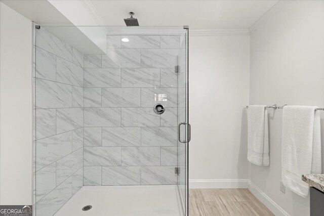 bathroom with ornamental molding, hardwood / wood-style floors, and a shower with shower door