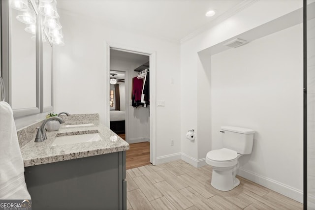 bathroom with ceiling fan, vanity, toilet, ornamental molding, and hardwood / wood-style floors